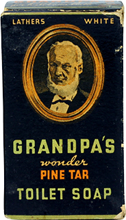 Vintage black soap box with a portrait of an elderly bearded man. Text reads: Grandpa’s Wonder Pine Tar Toilet Soap. Lathers White. Gold, green, and white lettering on a dark background.