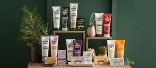 Display of assorted Grandpa Soap Co. natural personal care products, including soaps, body washes, shampoos, and conditioners, arranged on wooden stands with small plants against a green background.