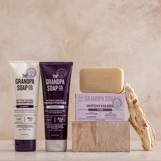 The Witch Hazel Collection Bundle from The Grandpa Soap Co. is displayed on a stone block beside wood, set against a neutral background.